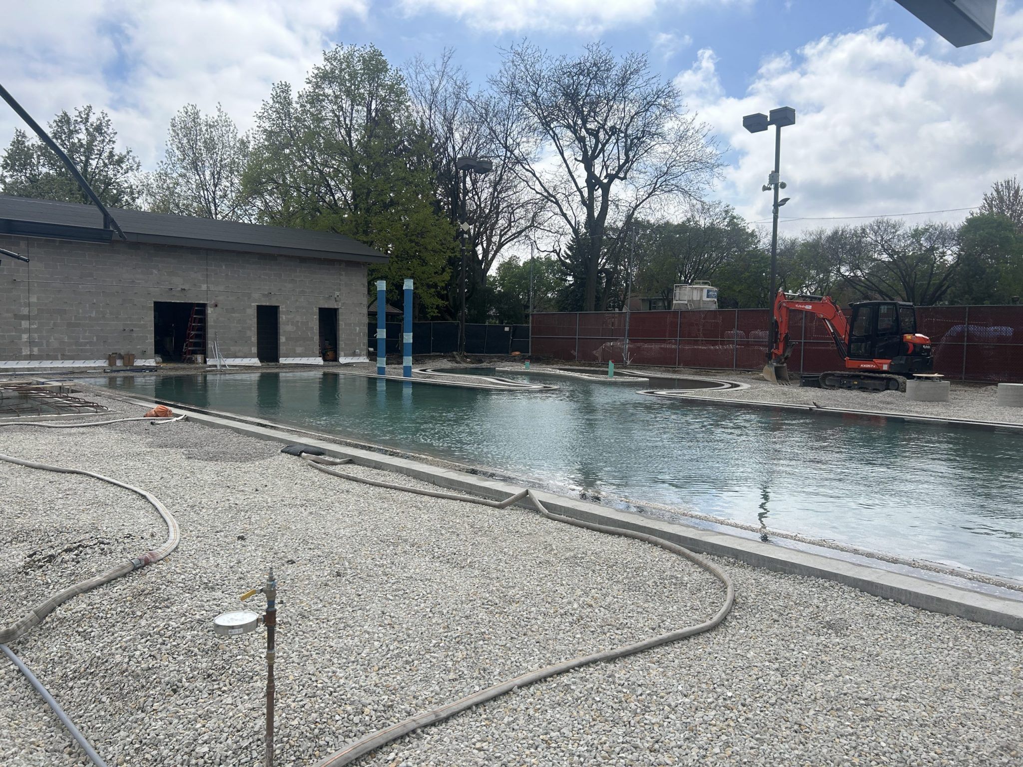 Construction of Rehm Park & Pool, showing a partially filled pool, a building under construction, and an excavator.