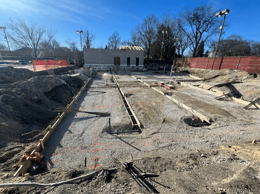 Rehm Park & Pool construction site with foundation forms and rebar in place, and a building under construction in the