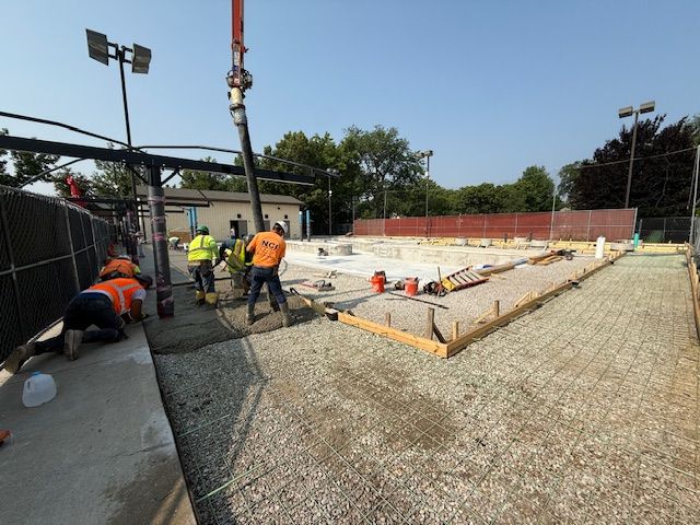 Construction workers pour concrete into a pool basin at Rehm Park & Pool using a concrete pump.