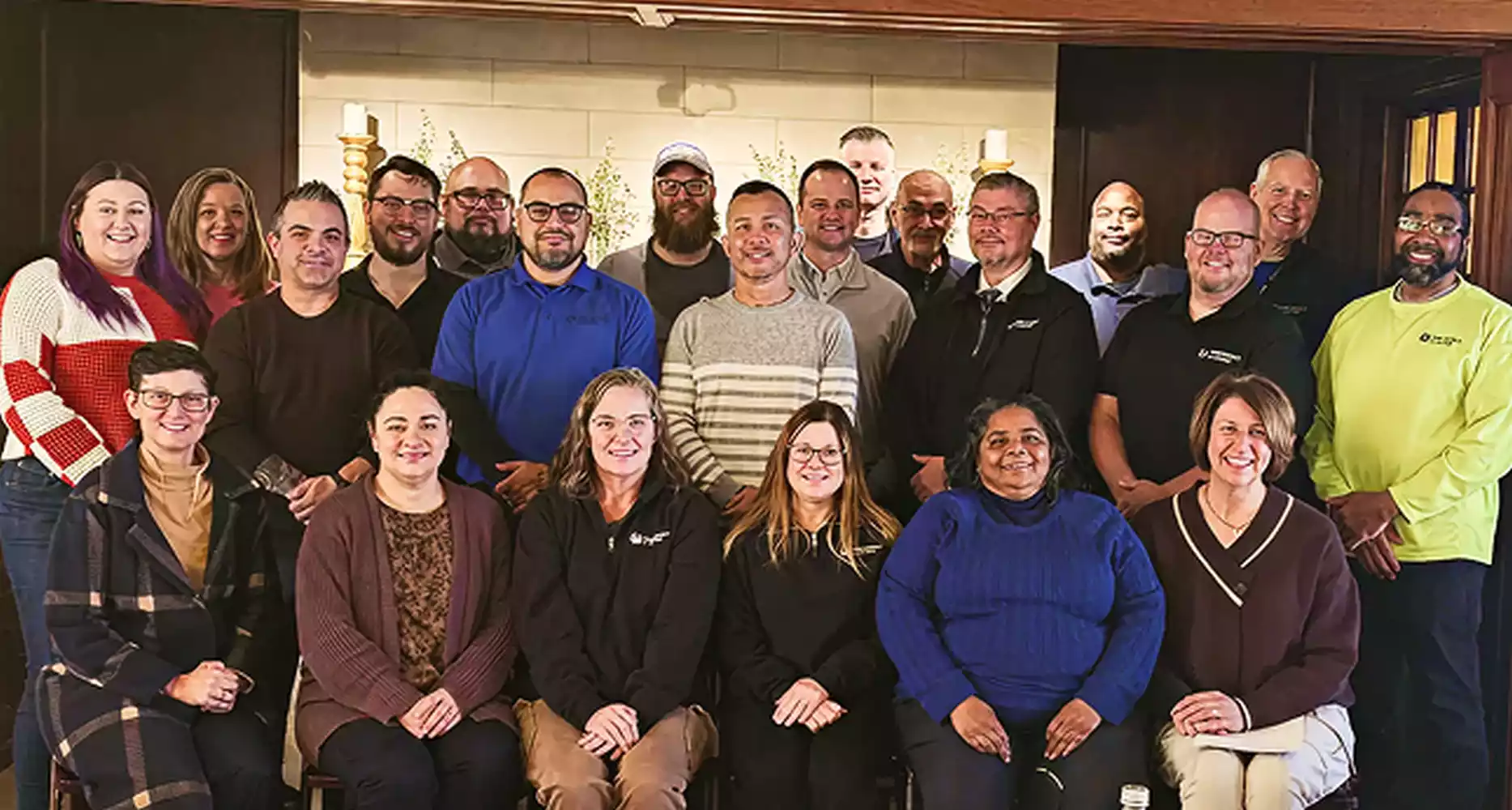 A diverse group of approximately 20 employees pose for a group photo, smiling at the camera.