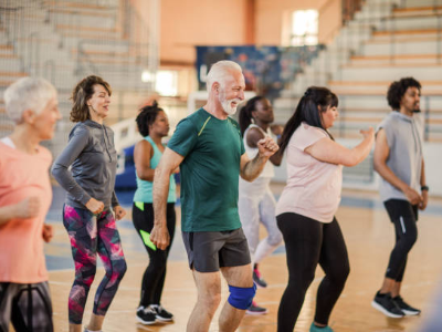 Diverse group of adults participating in a dance fitness class in a gymnasium.