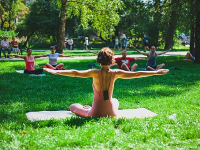 Group practicing yoga outdoors in a park, led by an instructor in the foreground.