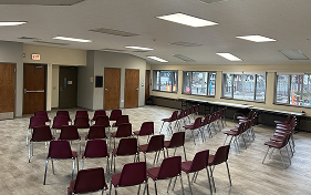 Chairs arranged in a circle and rows in a spacious room with windows and tables.