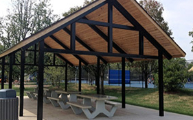 Open-air picnic shelter with a wood-paneled roof and concrete picnic tables underneath. Suitable for park rentals.