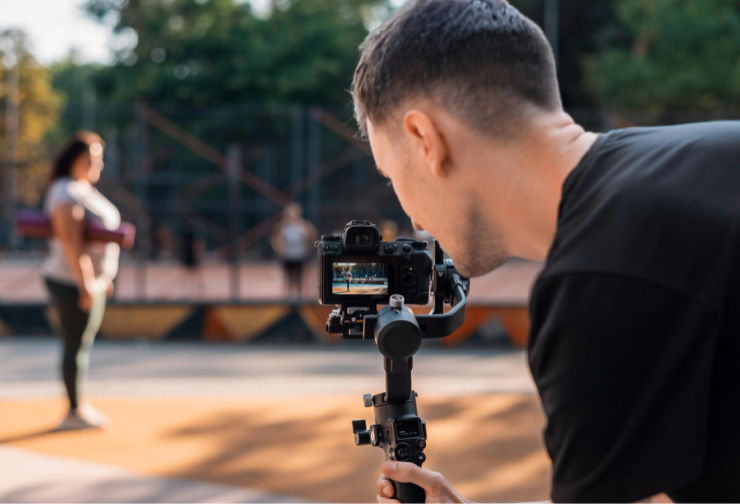 Videographer filming a woman holding a yoga mat outdoors.