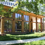 Modern wooden building with large windows, surrounded by green grass and trees. Part of the "Nature at Austin Gardens