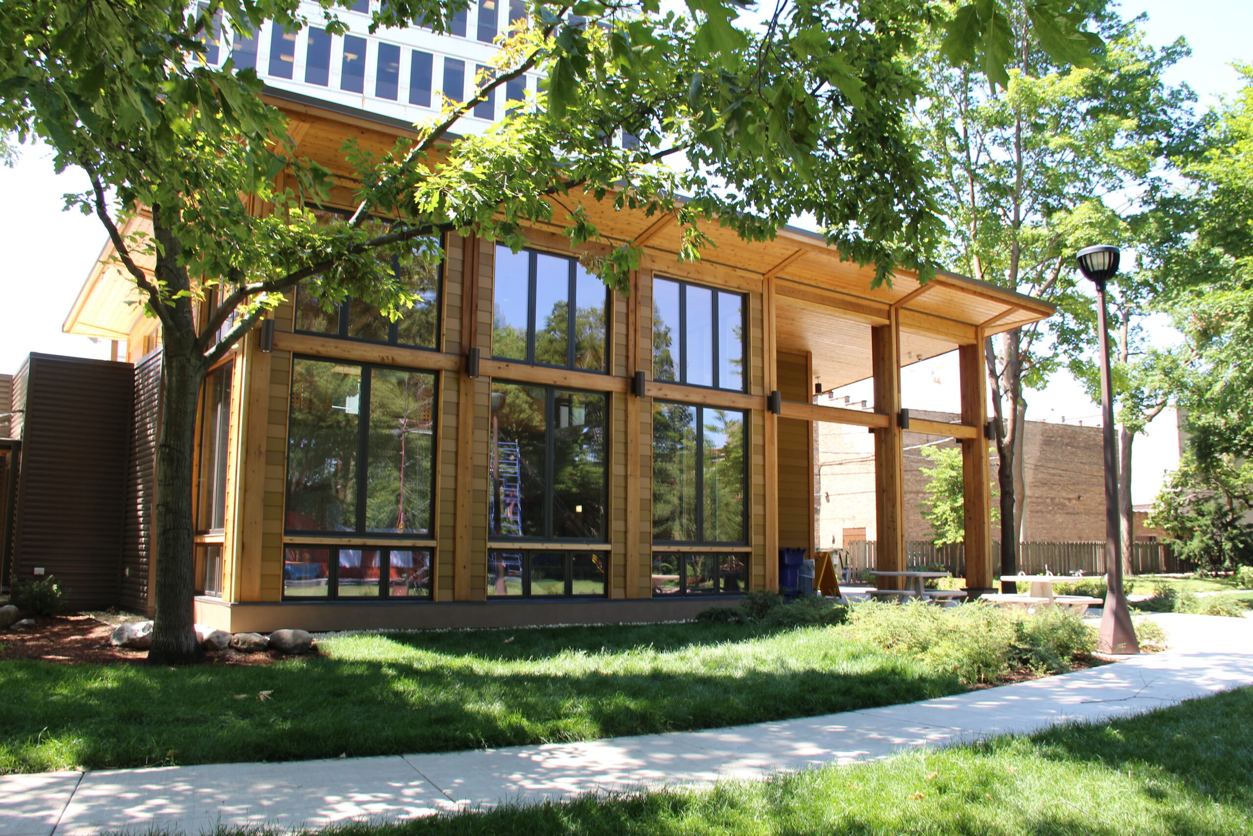 Modern wooden building with large windows, surrounded by green grass and trees. Part of the "Nature at Austin Gardens