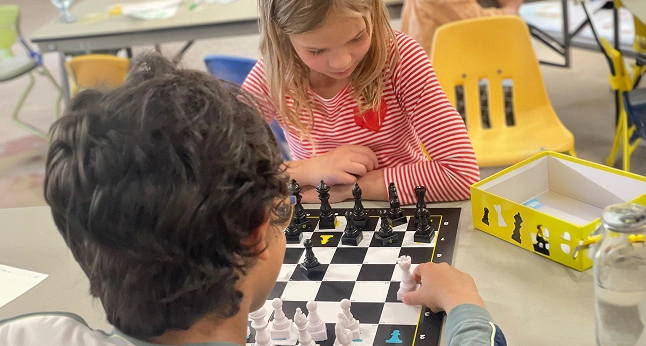 Two children, a boy and a girl, focus intently on a chessboard as they play a game of chess.