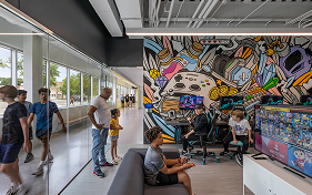 Youth and adults observe a vibrant esports room with gaming stations and a large mural.