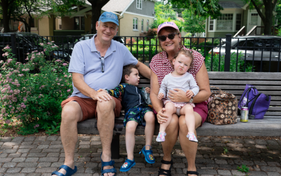 Family smiling for a picture while sitting on a bench at a park.