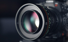 Close-up of a professional camera lens with "85" marked on the barrel, reflecting colorful light.