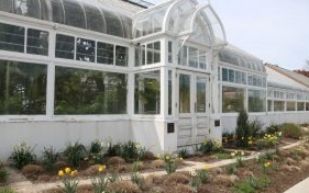 Exterior of the Oak Park Conservatory, a white greenhouse with glass panes and an arched entrance, surrounded by landscaping