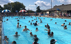 Crowded outdoor swimming pool with many people of all ages enjoying the water on a sunny day.