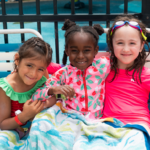 three girls wrapped smile at the camera while sitting on some pool chairs