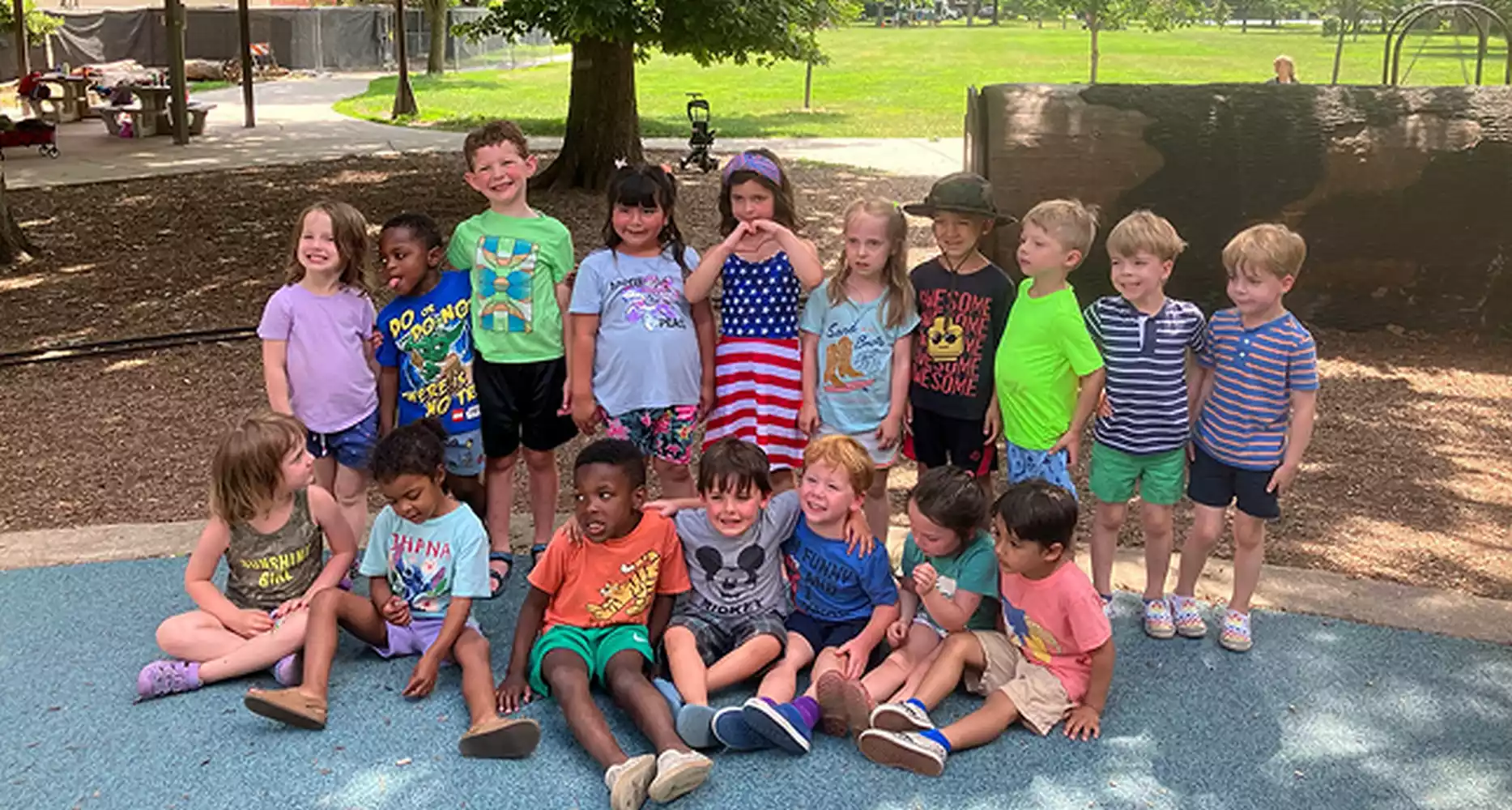 A diverse group of children posing for a photo on a playground. Some are standing, others sitting.