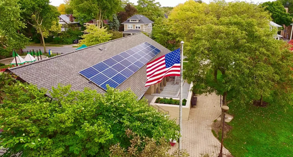 A building roof with solar panels and an American flag flying nearby, surrounded by trees.