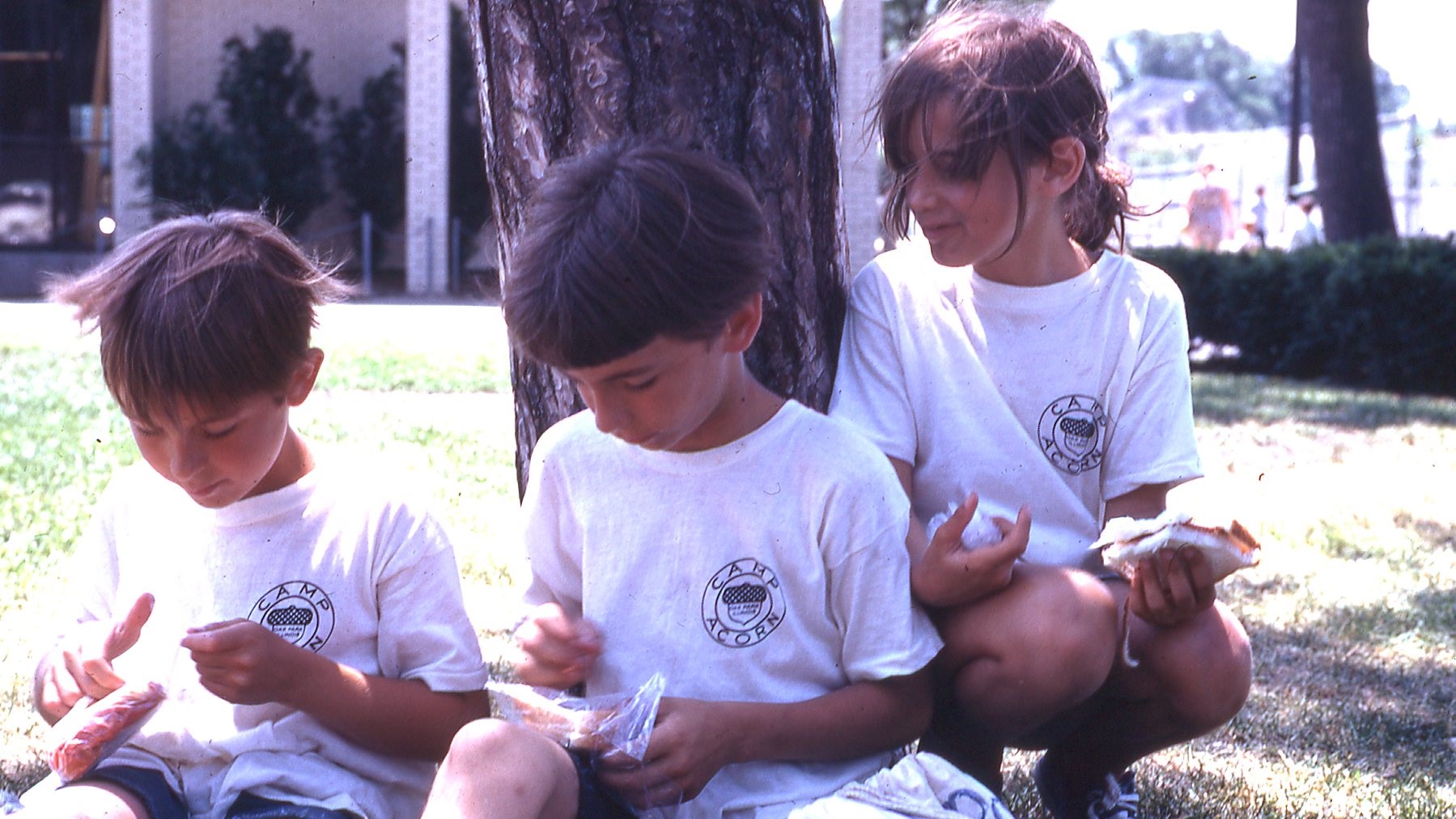 three kids in white tshirts with Camp Acorn written on them eat lunch - photo from 1968