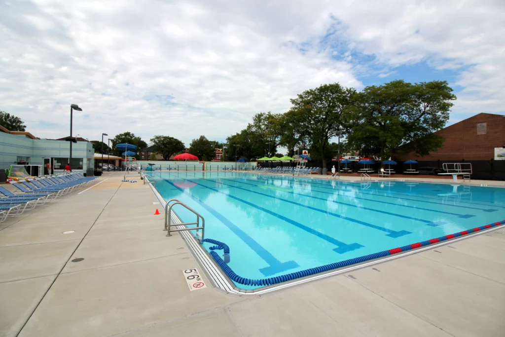 An outdoor swimming pool with multiple lanes, diving boards, lounge chairs, and umbrellas at the Ridgeland Common Recreation