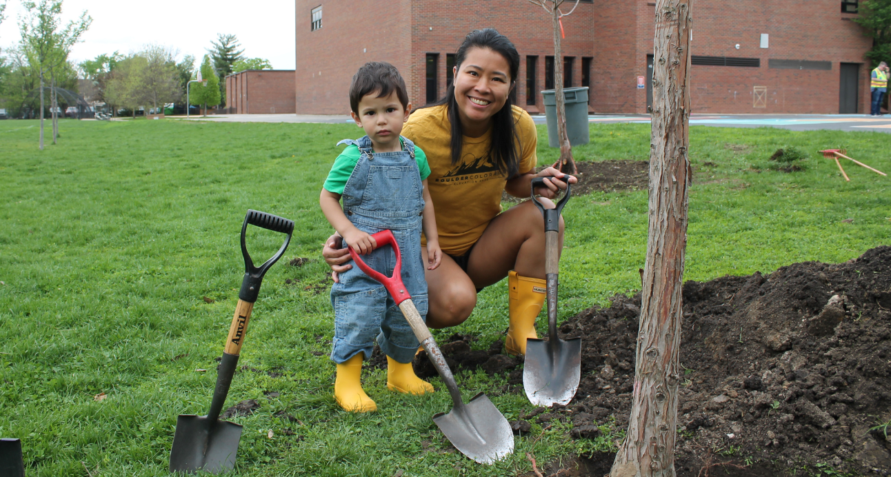 mom and son hold shovels next to a newly planted tree