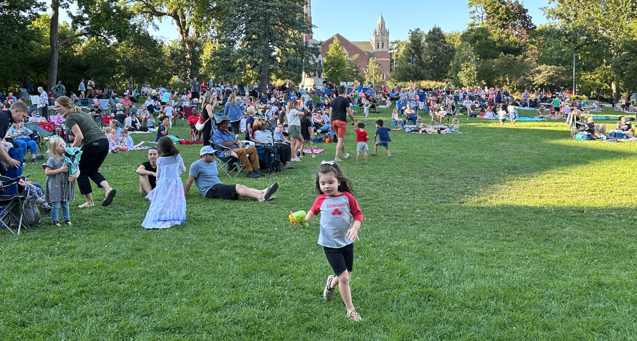 Young girl runs in Scoville Park with crowds of families seated in the background