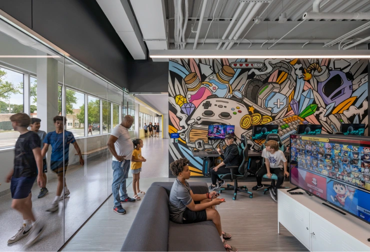 Children and adults in a modern esports lounge with vibrant gaming-themed mural and multiple gaming stations.