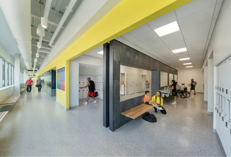 People of diverse ages and abilities use a modern locker room with accessible stalls, sinks, and benches.