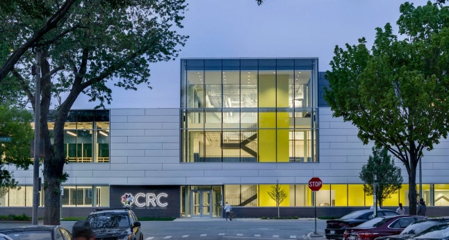 The Community Recreation Center features a modern facade with large glass windows revealing a bright yellow staircase and