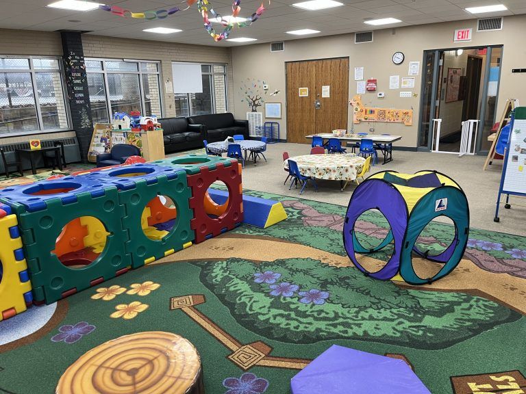 A colorful indoor playground area with large building blocks, a pop-up tent, and child-sized tables and chairs.