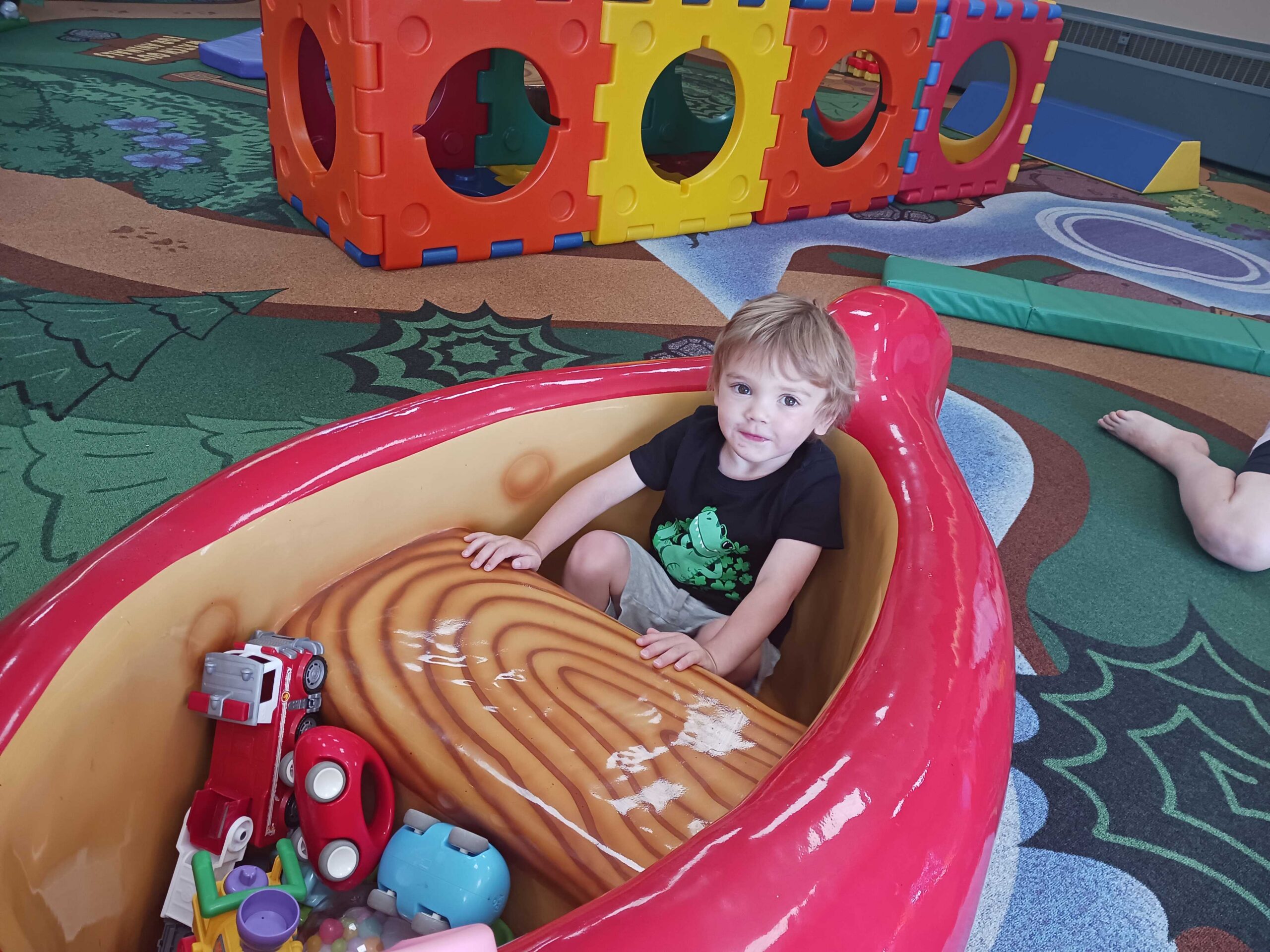 boy sits in large red canoe with toys