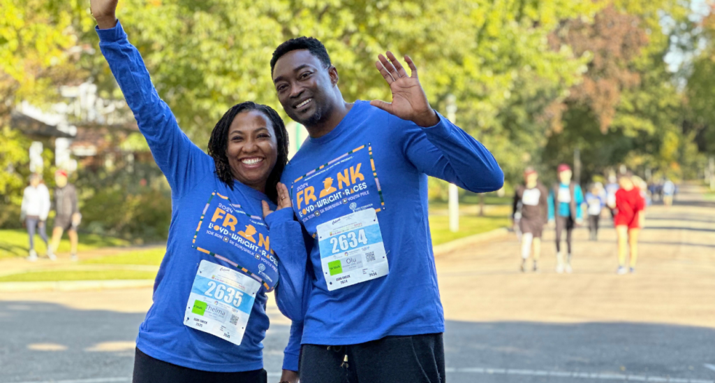 a couple in blue frank lloyd wright shirts wave to the camera