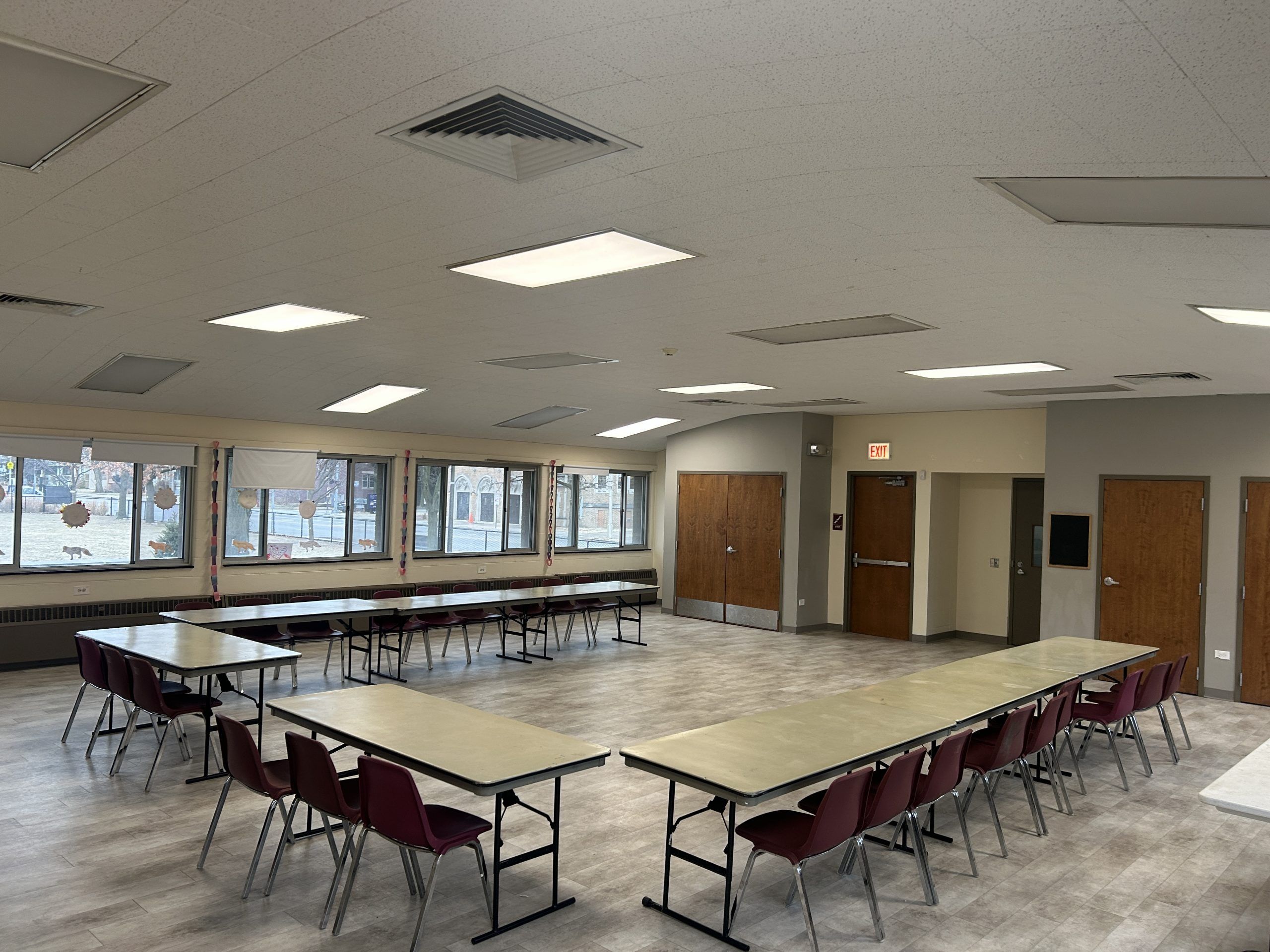 Tables and chairs in a large u shape set up in a spacious room with wood doors and large windows.