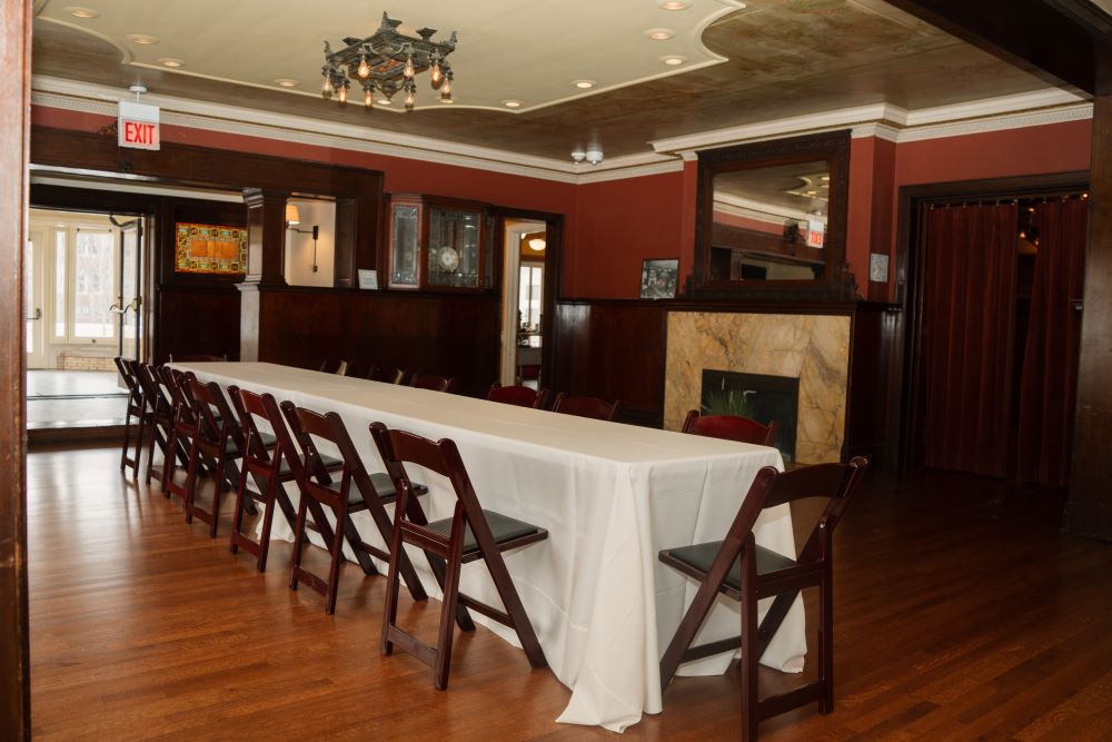 long table with white tablecloth and wood chairs set in room with painted ceilings and a fireplace