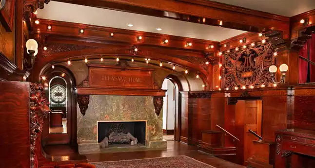 Interior of Pleasant Home featuring ornate wood carvings, a marble fireplace, and decorative lighting.