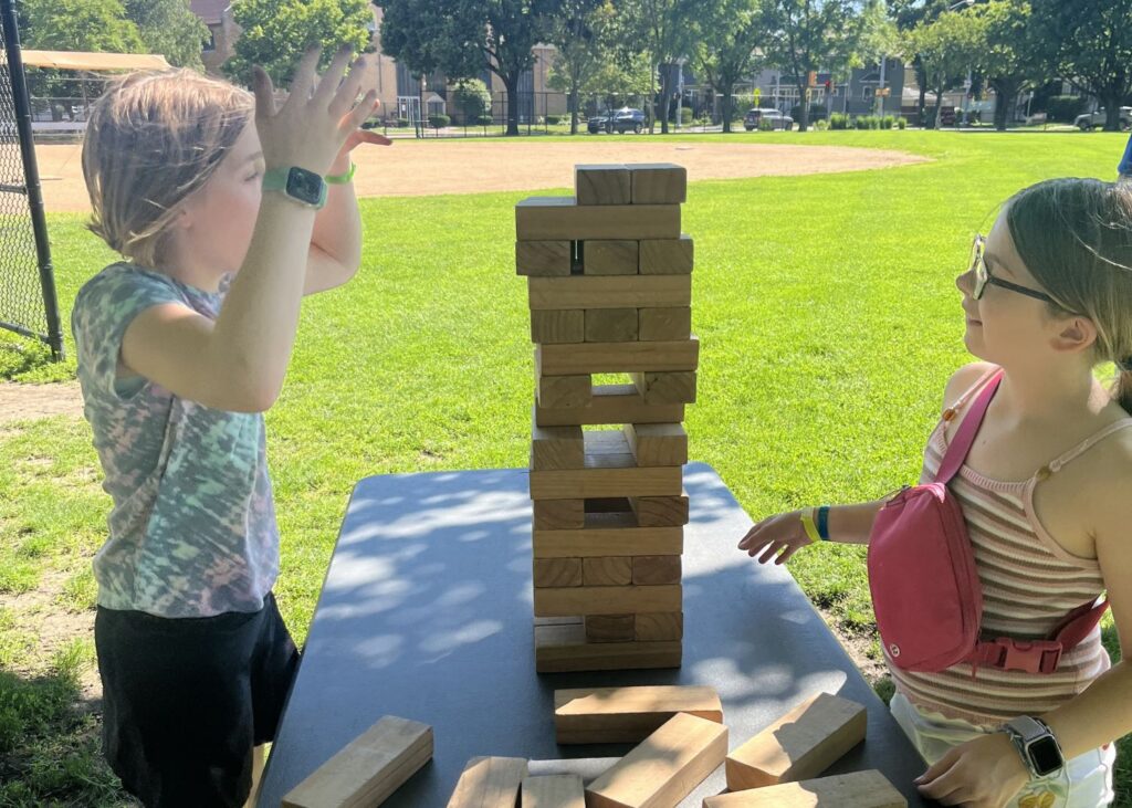 two girls face a jenga tower of wooden blocks