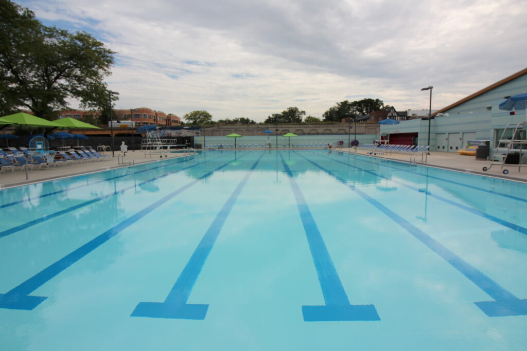 An outdoor swimming pool with lane markers and lounge chairs under umbrellas.