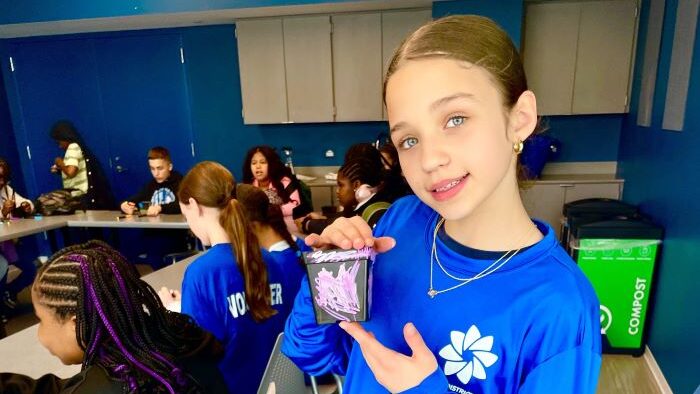 girl in blue pdop shirt holds up a painted flower pot with other students in background