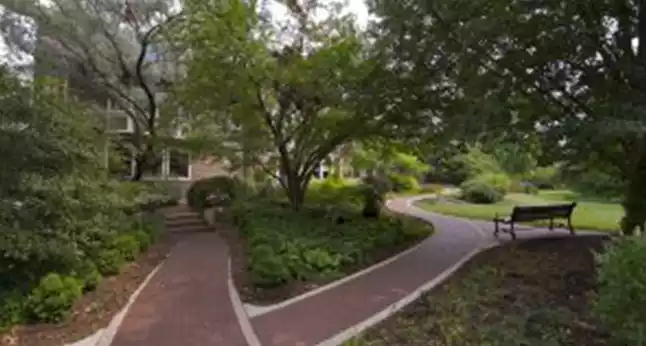 Winding paths through a lush garden with a bench, leading towards Cheney Mansion.