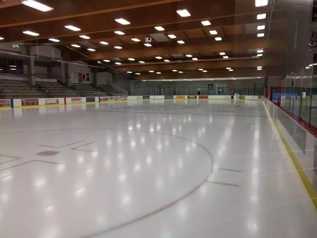 Interior view of an empty ice hockey rink with spectator seating and overhead lighting.