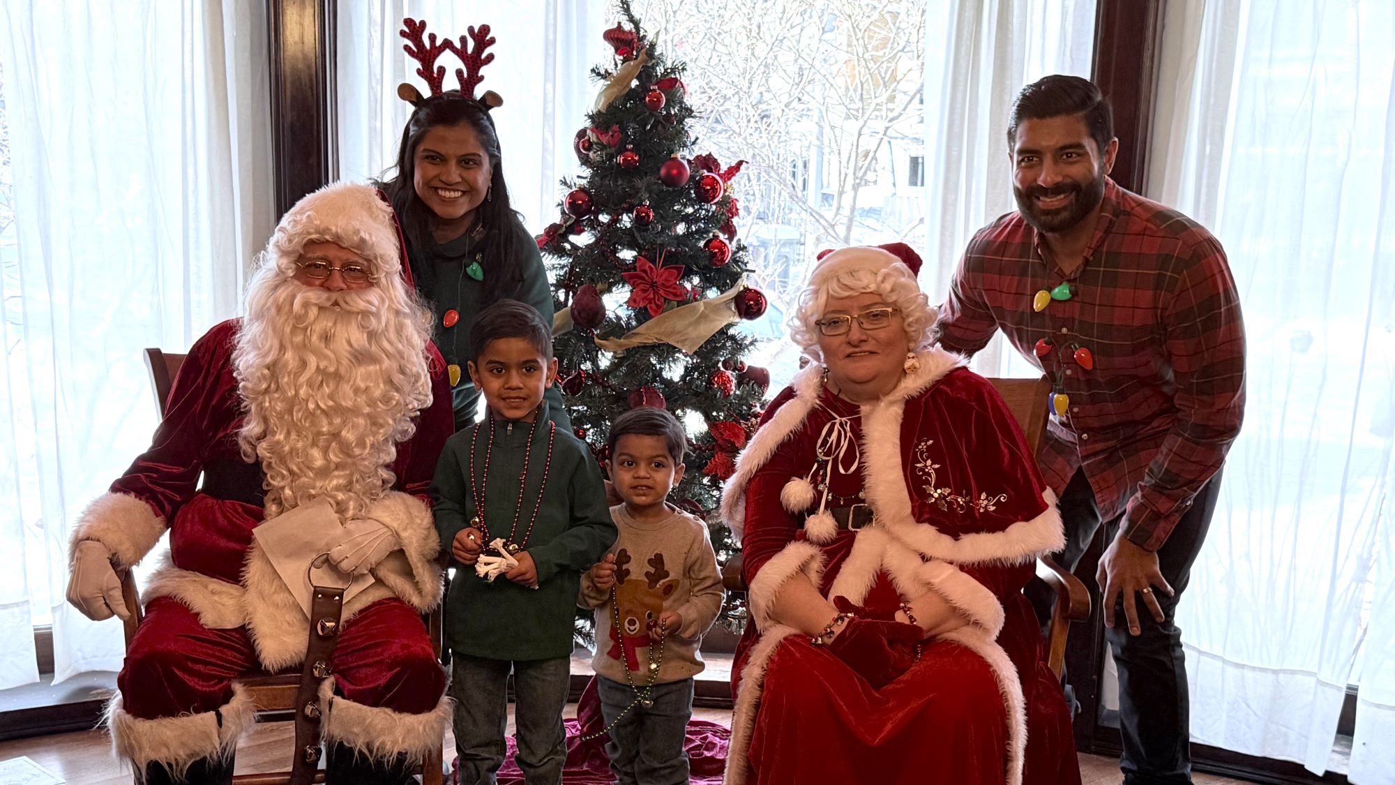 two parents and two kids dressed in holiday attire pose for a picture with santa and mrs. claus